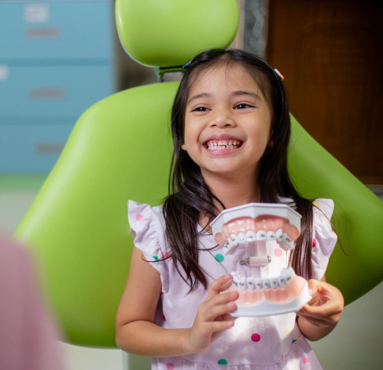 A little girl holding a teeth model and smiling